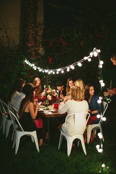 a group of people sitting around a table with lights strung over the top of it