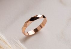 a rose gold wedding ring on top of a white furnishing area with feathers