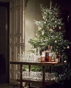 a bar cart with wine glasses and bottles on it in front of a christmas tree