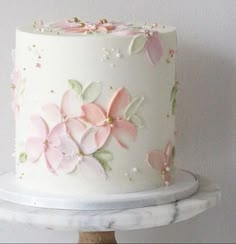 a white cake decorated with pink flowers and butterflies on top of a wooden stand next to a wall