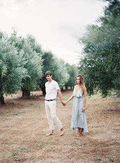 a man and woman holding hands in an olive grove