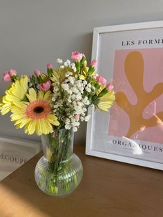 a vase filled with flowers sitting on top of a table next to a framed poster