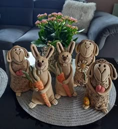 four ceramic rabbits holding carrots on top of a table next to a vase with flowers