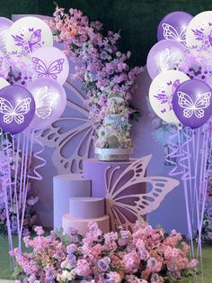 purple and white balloons with butterflies on them are in front of a cake surrounded by flowers