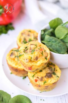 three muffins on a white plate with spinach and tomatoes in the background