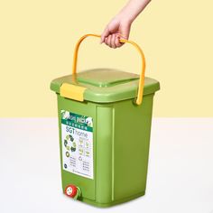 a hand holding a yellow handled handle on a green container