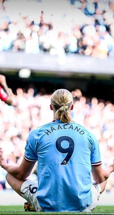 a soccer player sitting on the ground in front of a crowd with their hands together