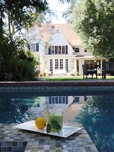 a glass of green juice sitting on top of a table next to a swimming pool