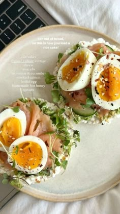 an open faced sandwich with hard boiled eggs on top and bacon in the middle is sitting on a plate next to a laptop