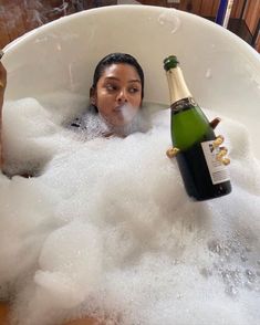 a woman in a bathtub with bubbles and a bottle of champagne next to her