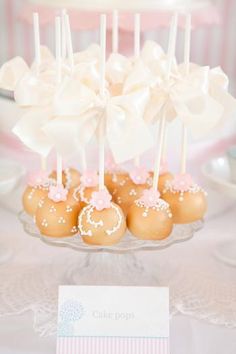 some cake pops are on a plate with white frosting and pink bowknots