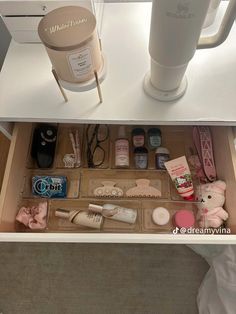 an open drawer with various items in it on a white counter top next to a cup