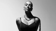 a woman with braids in her hair and wearing a black bra top, standing against a white background