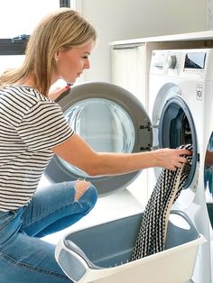 a woman is doing laundry in front of a washing machine