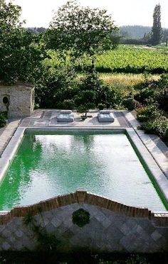 an outdoor swimming pool surrounded by greenery and stone walls, with two hot tubs in the middle