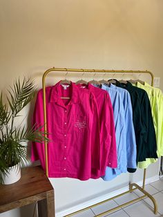 four shirts are hanging on a rack next to a potted plant