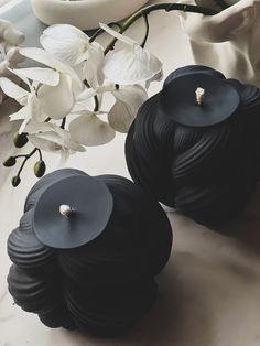 two black candles sitting on top of a table next to flowers and a vase with white orchids