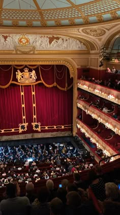 an auditorium filled with lots of people sitting on top of red seats and looking up at the stage