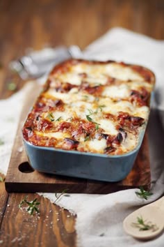 a casserole dish with cheese and herbs on a cutting board next to spoons