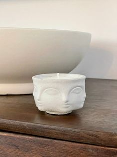 a white candle sitting on top of a wooden table next to a bowl and plate