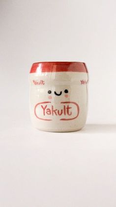 a small cup with a face on the side and words yakult written in red