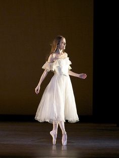 a woman in white dress standing on stage with one leg up and her arms out