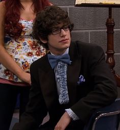 a young man in a suit and bow tie sitting on a chair next to a woman