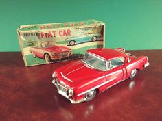 a red toy car sitting on top of a wooden table next to a tin box