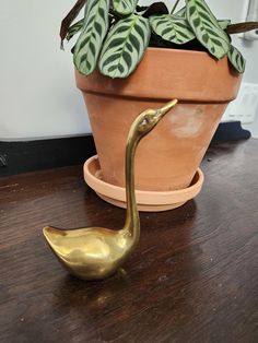 a brass bird figurine sitting on top of a wooden table next to a potted plant