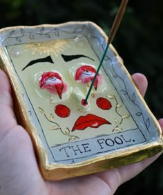 a hand holding a small ceramic clock with red lips and eyebrows on it's face