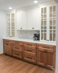 an empty kitchen with white cabinets and wood flooring, along with a coffee maker on the counter