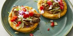 two small pizzas with meat and veggies are on a blue plate, ready to be eaten