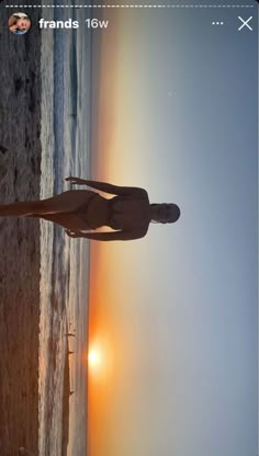 a woman standing on top of a sandy beach next to the ocean at sun set