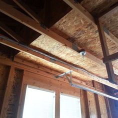 an unfinished room with wooden walls and exposed pipes on the ceiling, along with two windows