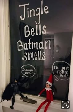 an elf is sitting on the window sill next to two toy bats and a batman