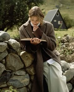 a woman sitting on top of a stone wall next to a pile of rocks holding a book