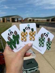 the person is holding three different earrings in front of their face and one has four green bows on them