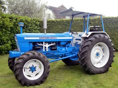 a blue tractor parked on top of a lush green field next to a tall hedge