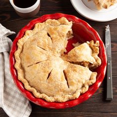 a pie sitting on top of a red plate next to a knife and cup of coffee