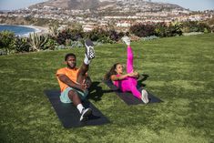 two people doing yoga on their stomachs in the middle of a grassy area with a city view behind them