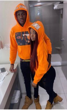 a man and woman in orange hoodies standing next to each other near a sink