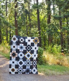 a black and white quilt sitting on the side of a road in front of trees