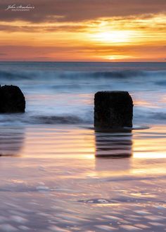 the sun is setting over the ocean with rocks in the foreground and waves on the water