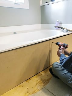 a person sitting on the floor with a drill in their hand and a sink behind them