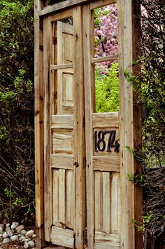 an old wooden outhouse sitting in the middle of some bushes and trees with a number on it