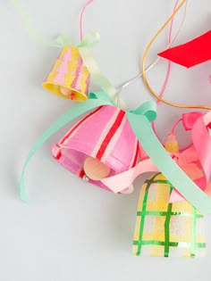 colorful paper decorations hanging from strings on a white surface with ribbons and bows attached to them