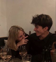 a man and woman sitting at a table with wine glasses in front of their faces