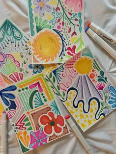 four colorful cards with markers on them and one has an umbrella painted on it, the other has flowers