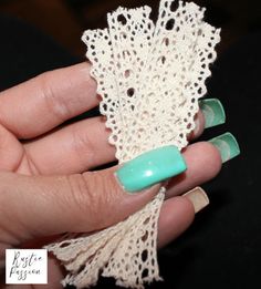 a hand holding a piece of lace with green and white nail polishes on it