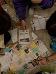 three children sitting on the floor looking at pictures and papers that they are holding in their hands